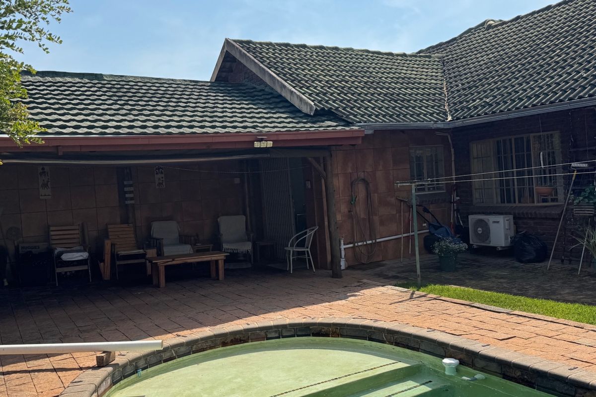 Rear exterior view featuring a paved patio area, covered veranda, and swimming pool set against the main house structure.