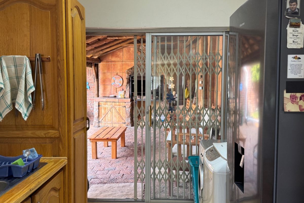 Kitchen area featuring built-in wooden cabinetry, leading through a sliding security gate to a covered outdoor patio with a built-in braai.