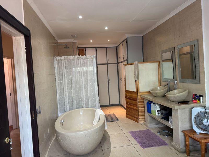 Spacious bathroom featuring a freestanding bathtub, dual vessel sinks on a concrete vanity, and extensive built-in storage cabinetry with neutral wall tiling.