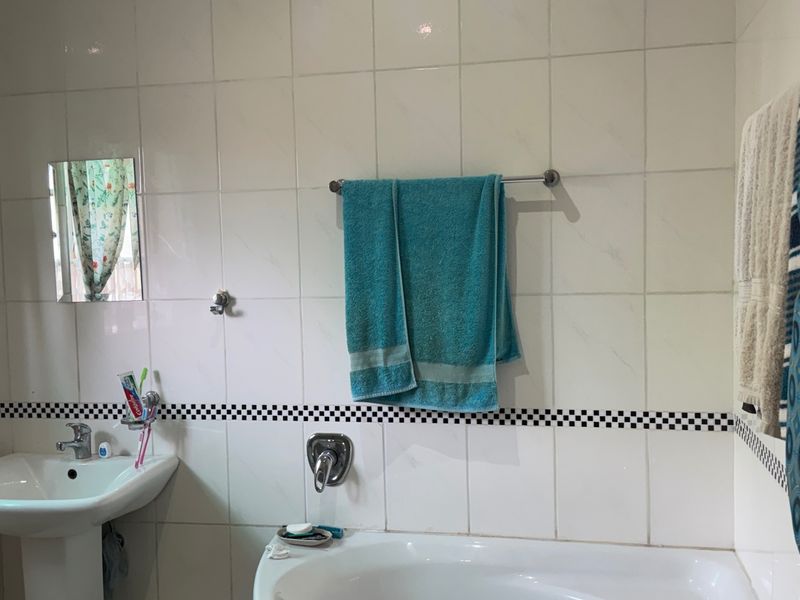 A functional bathroom featuring a pedestal washbasin, built-in bathtub, and classic white wall tiling with a decorative checkered border.