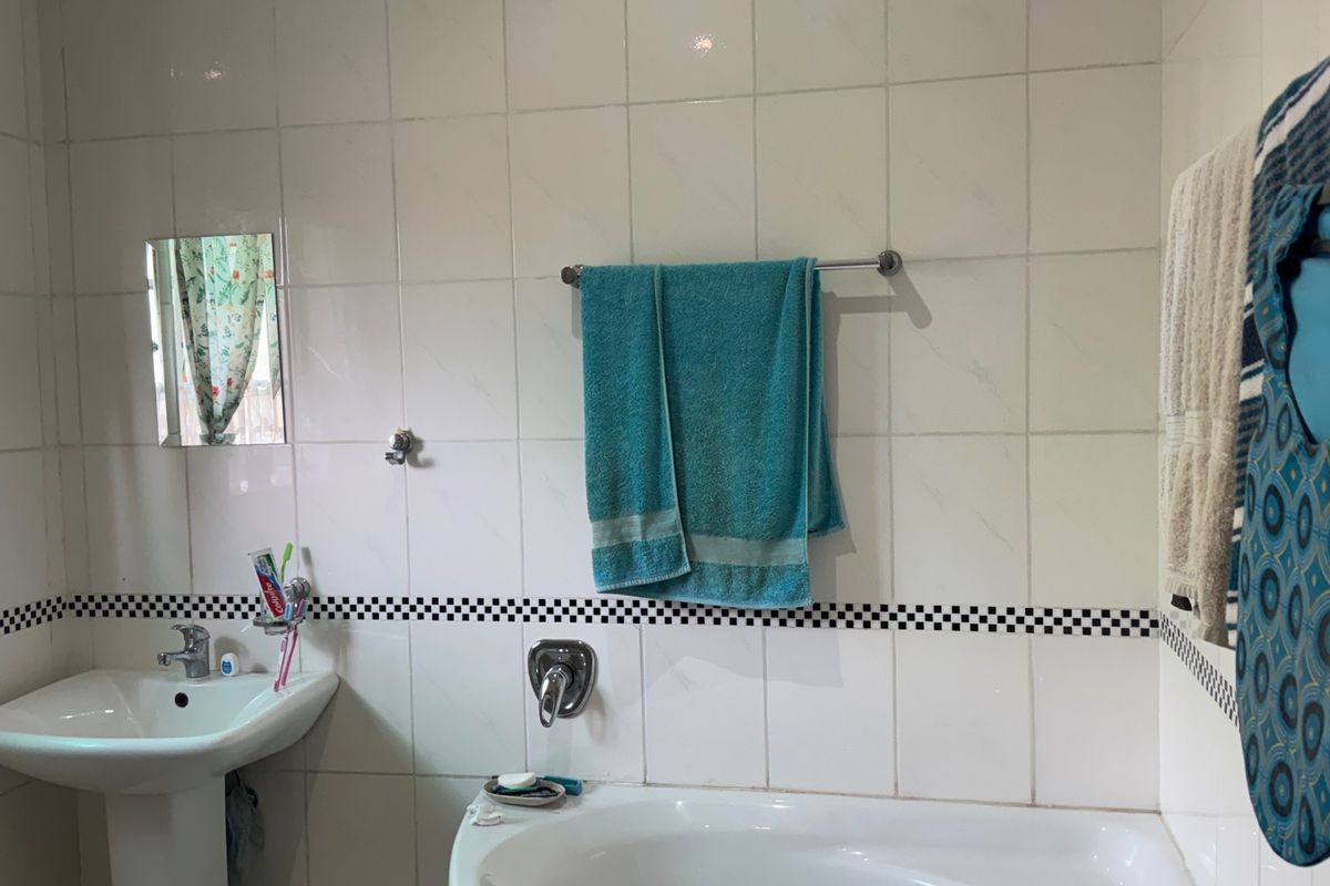 A functional bathroom featuring a pedestal washbasin, built-in bathtub, and classic white wall tiling with a decorative checkered border.