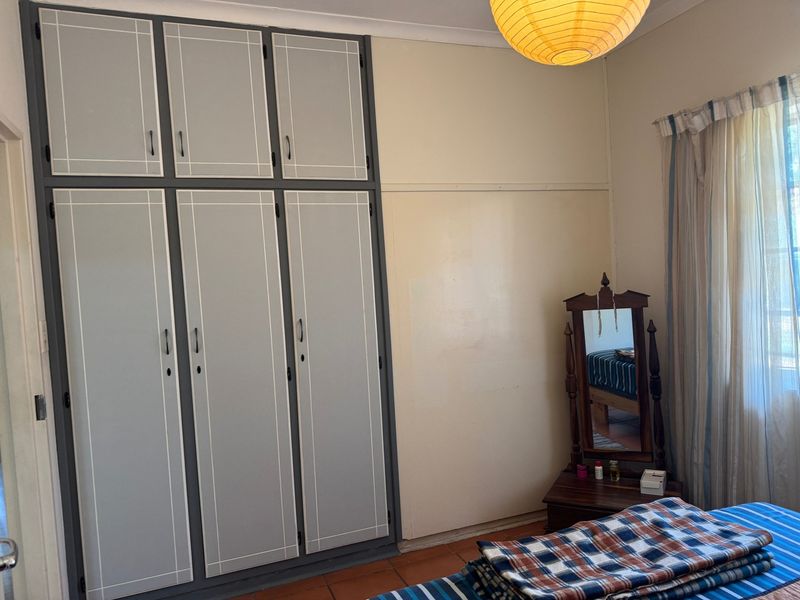A bedroom featuring built-in cupboards with a painted finish and tiled flooring, offering functional storage space.