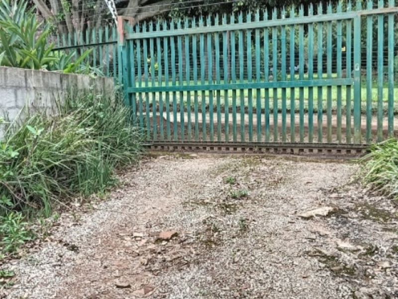 A gated entrance to the property featuring a metal sliding gate, concrete block retaining wall, and a gravel driveway approach.