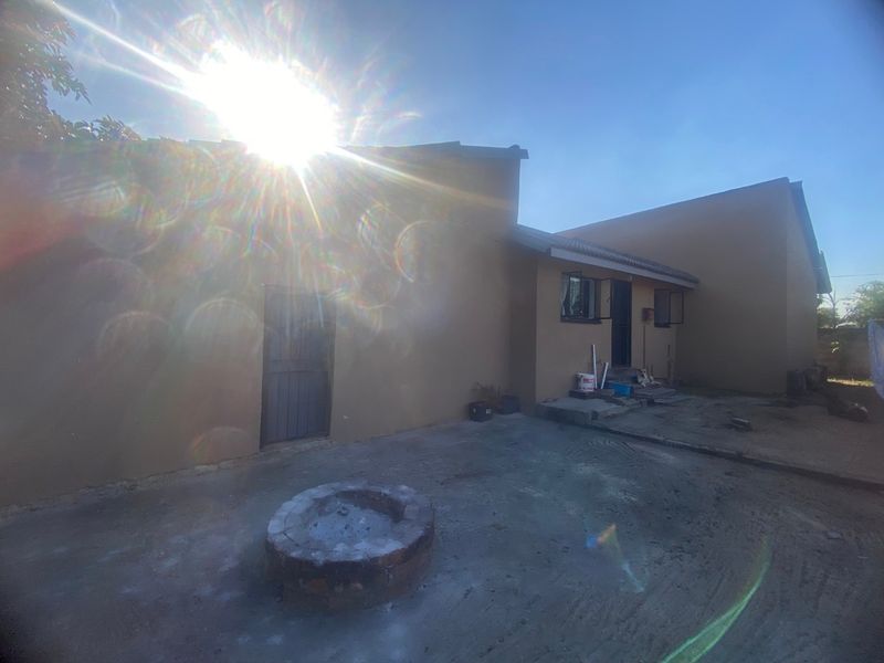 Rear exterior view of the property featuring a concrete patio area with a built-in brick fire pit and direct access to the house.