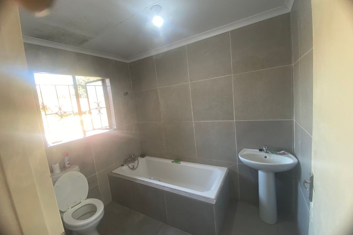 A functional bathroom featuring a bathtub, pedestal basin, and toilet with neutral wall and floor tiling.