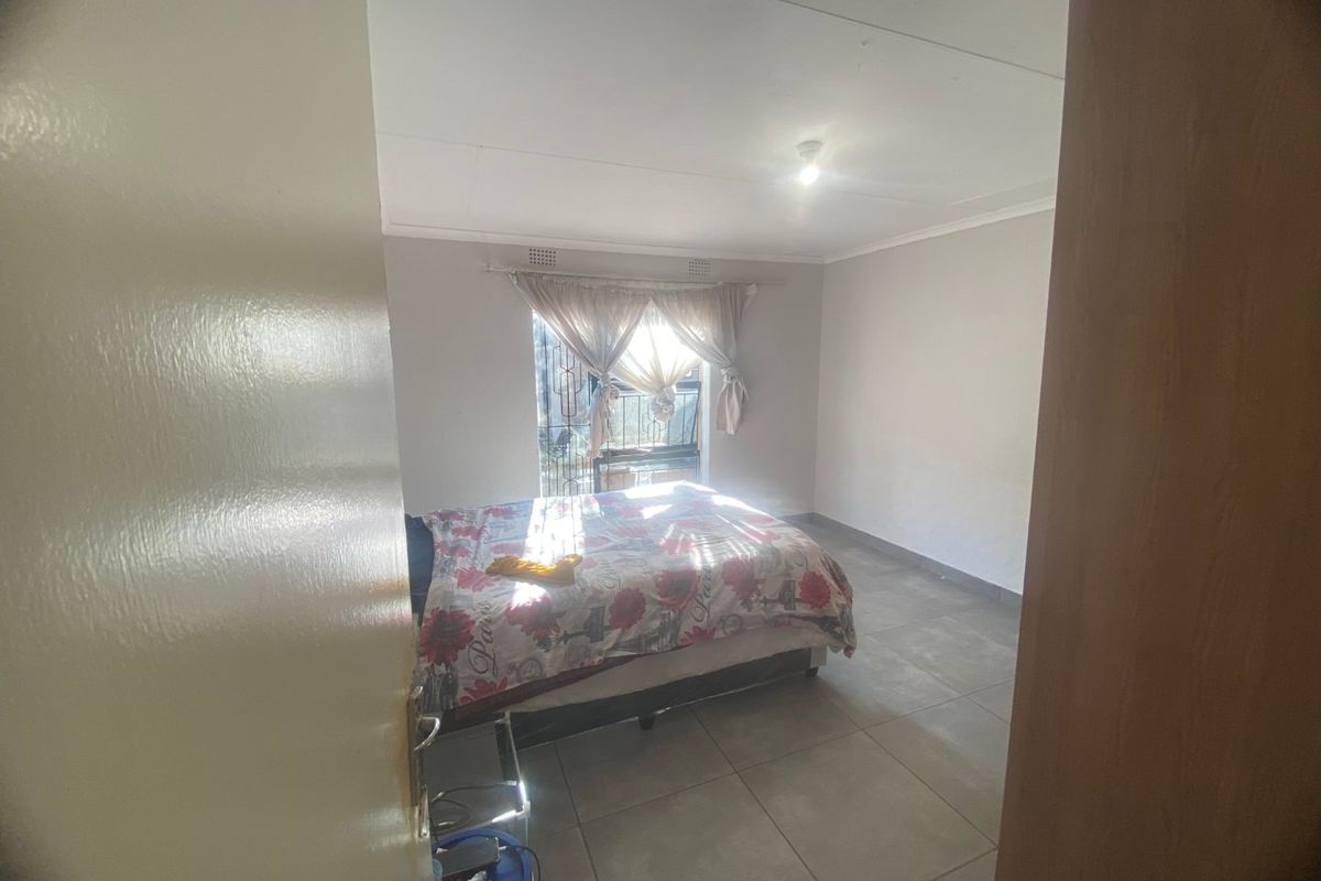 A bedroom featuring neutral wall finishes, large format floor tiles, and a window fitted with security bars.