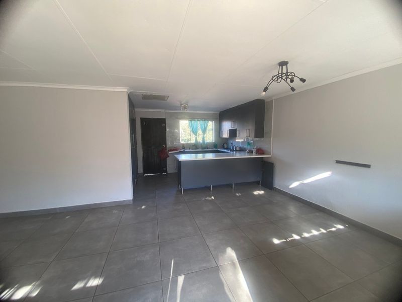 An open-plan living and kitchen area featuring modern dark cabinetry, a central kitchen island, and neutral tiled flooring throughout.