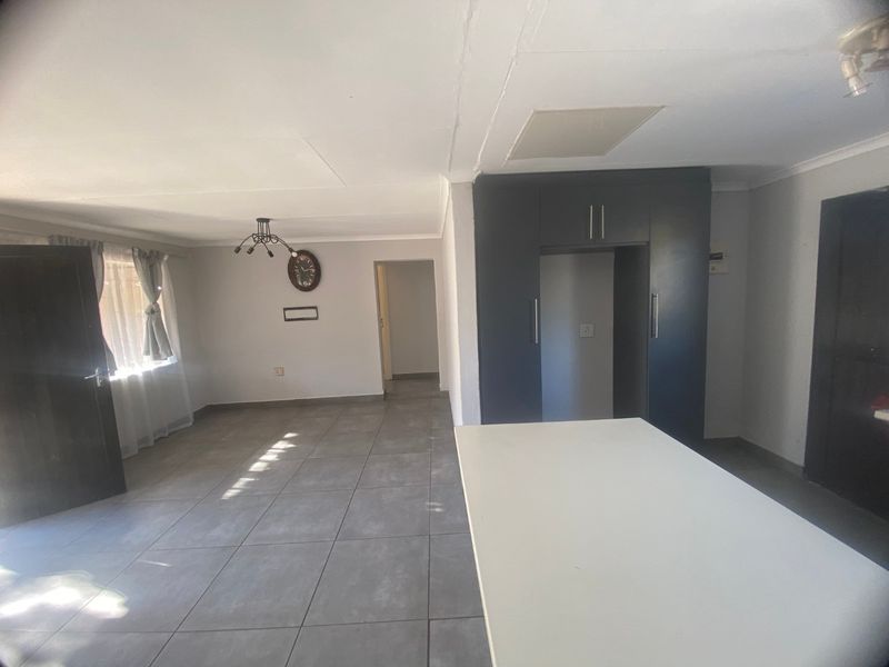 An open-plan living and kitchen area featuring large format floor tiles, built-in dark cabinetry, and a central island, offering a clean, neutral canvas.