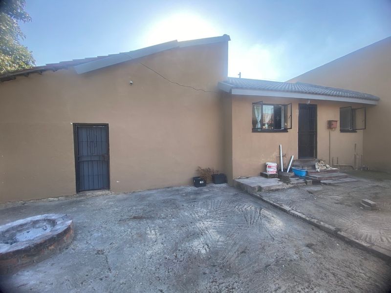 Rear exterior view of the property featuring a concrete paved area, security gates, and a brick fire pit.
