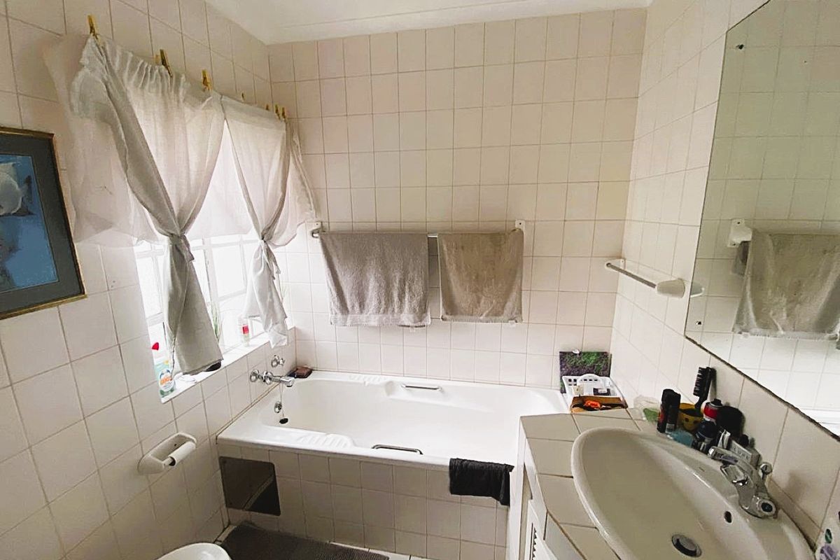 A dated bathroom featuring a built-in bathtub, vanity basin, and tiled finishes, offering potential for a modern renovation.
