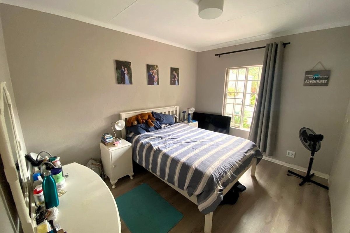 A functional bedroom featuring laminate flooring, a window with security bars, and neutral wall tones, offering a comfortable space for rest.