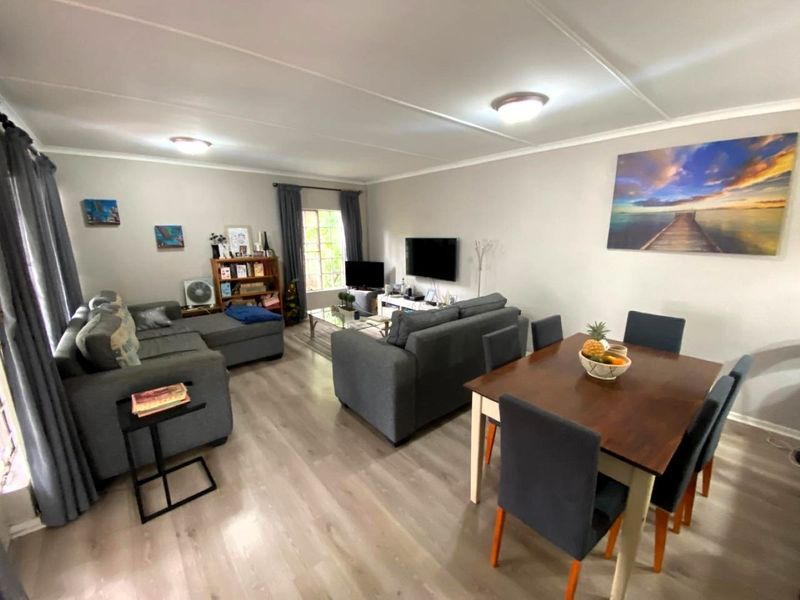 An open-plan living and dining area featuring light-toned laminate flooring, neutral wall finishes, and functional ceiling lighting.