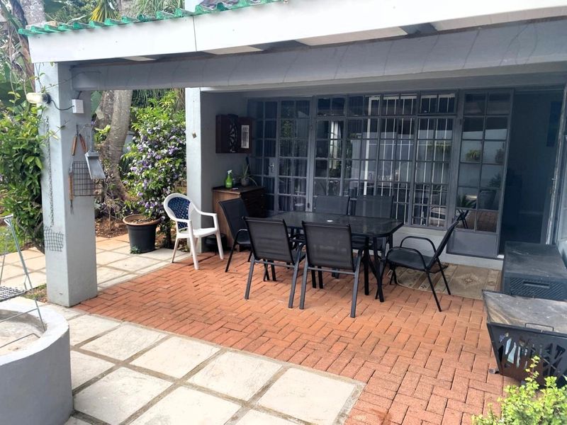 A covered outdoor patio area featuring brick and concrete paving, accessible through large steel-framed glass doors with security bars.
