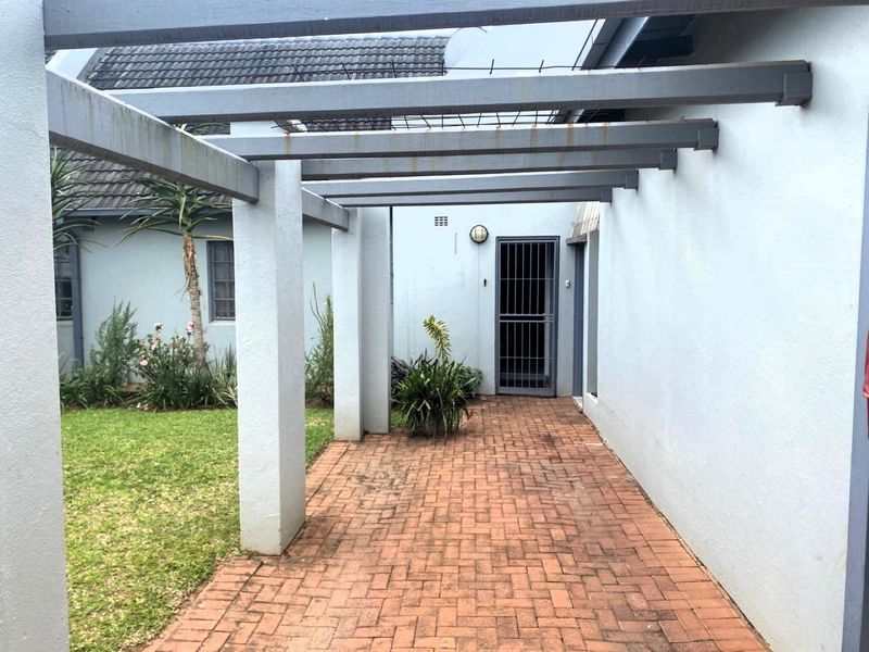 A covered patio area featuring brick paving and a pergola structure, providing a transition space between the garden and the home entrance.