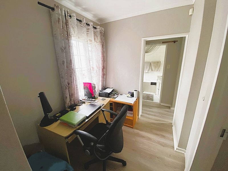 A functional home office space featuring laminate flooring and neutral wall finishes, with direct access to an adjacent bathroom.