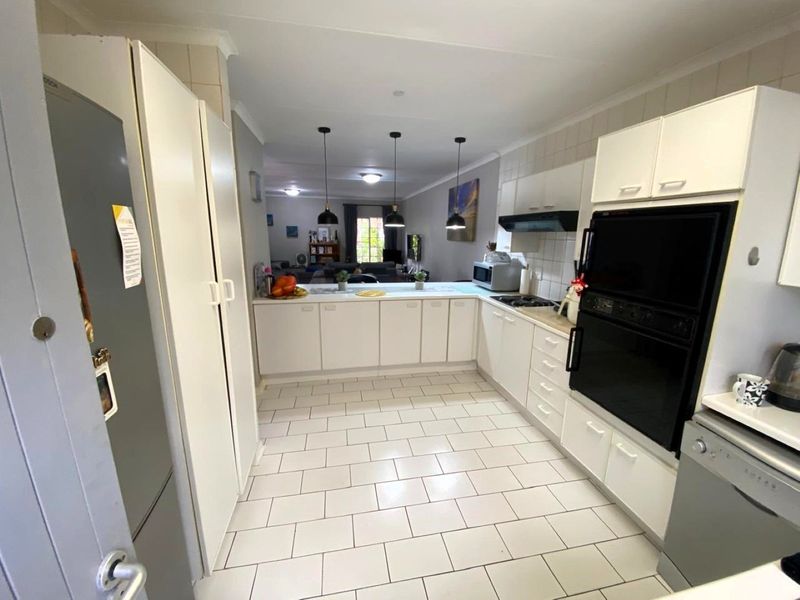 Open-plan kitchen featuring white cabinetry, tiled flooring, and built-in appliances, flowing seamlessly into the adjacent living area.