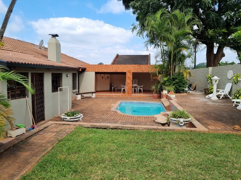 Outdoor entertainment area featuring a swimming pool, brick-paved patio, and a covered terrace with a chimney, set within a private garden.