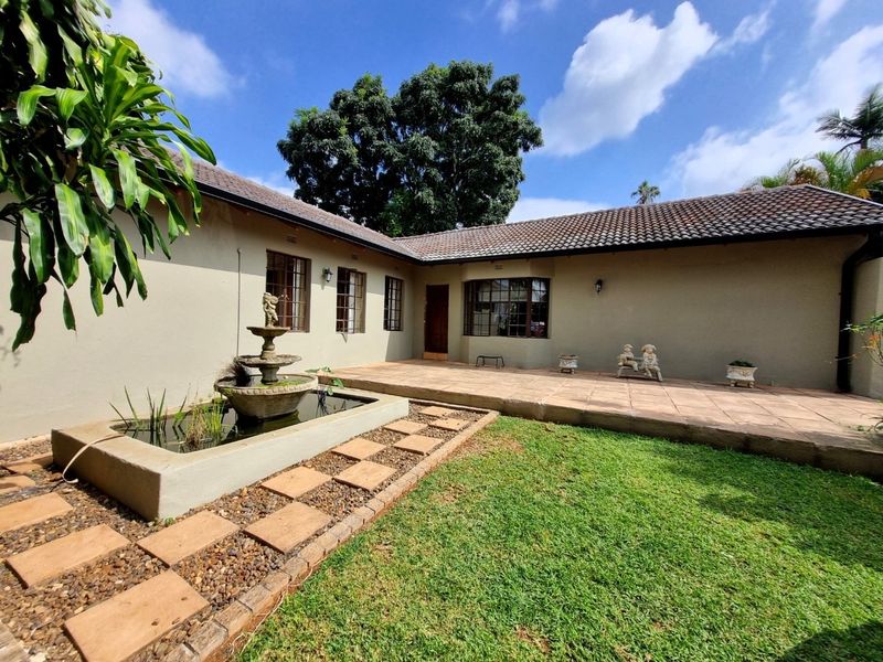A well-maintained rear exterior featuring a tiled patio, a decorative water feature, and a landscaped garden area with established trees.