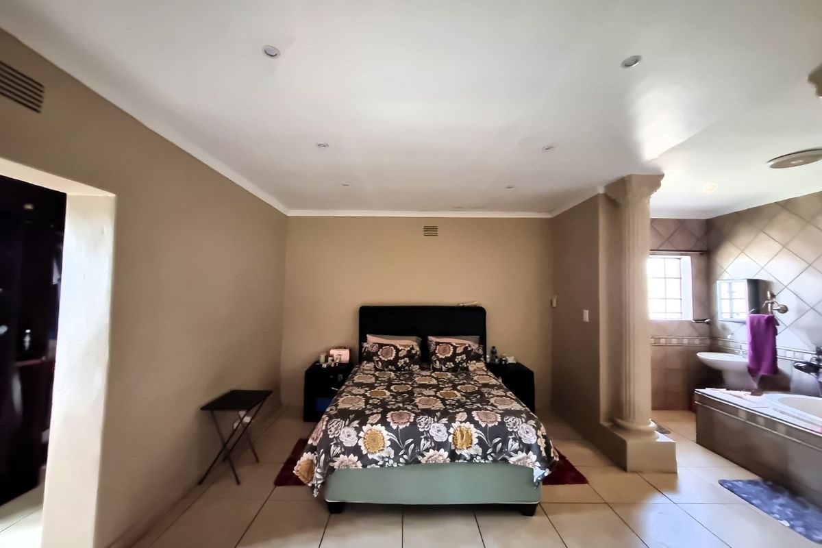 Spacious bedroom featuring tiled flooring, recessed lighting, and an open-plan en-suite bathroom area with a built-in bathtub and decorative column.