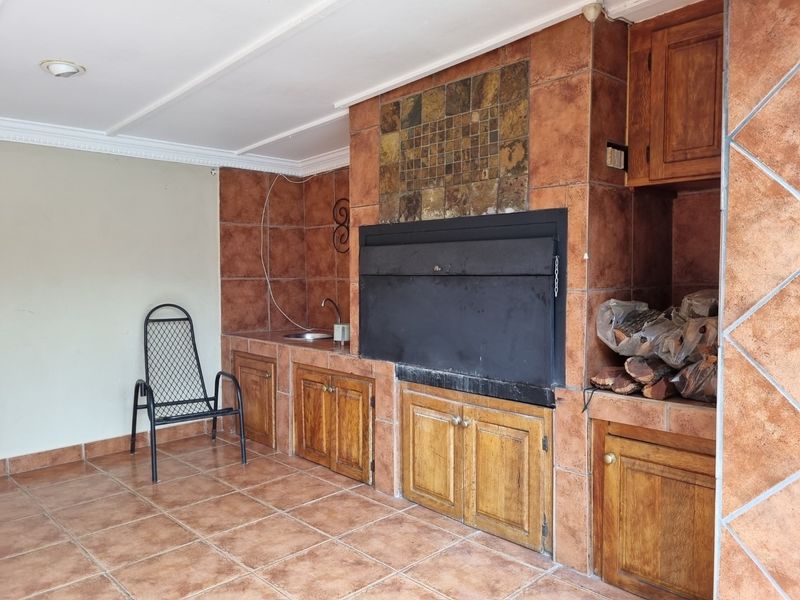 Covered patio area featuring a built-in braai, tiled flooring, and integrated cabinetry with a sink, ideal for outdoor entertaining.
