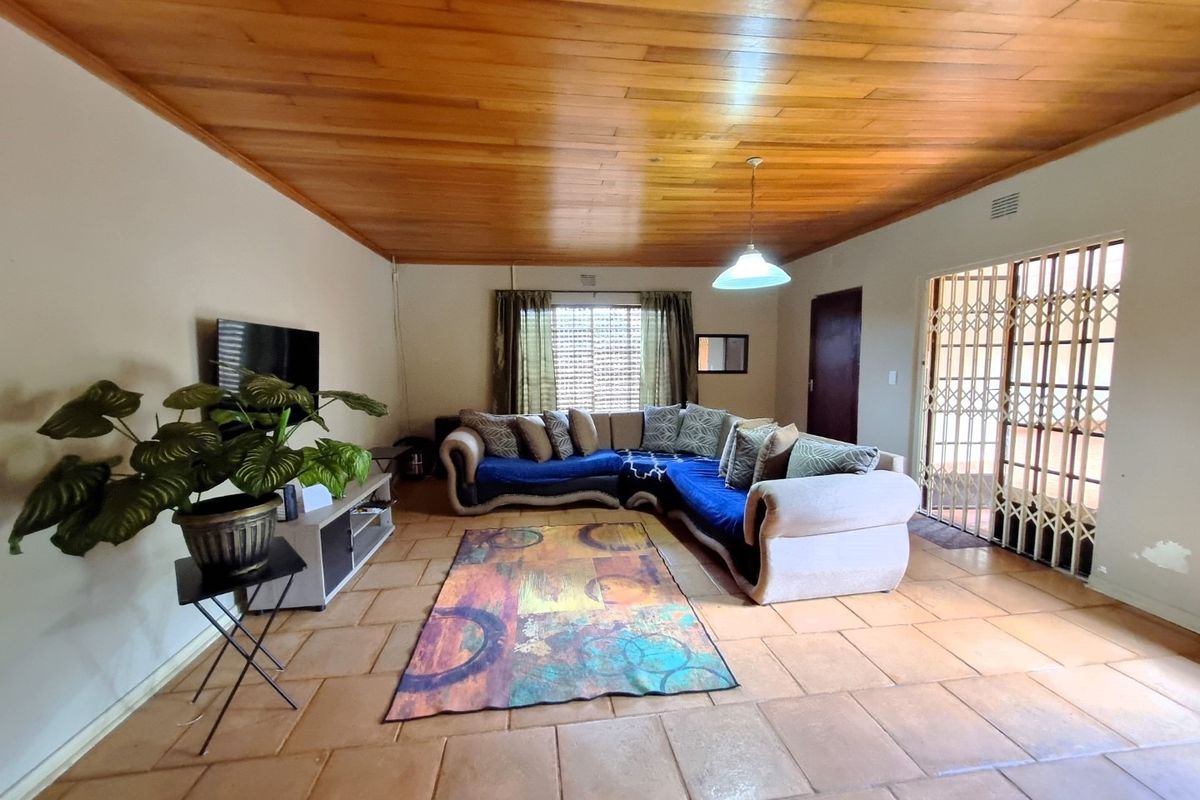 Spacious living room featuring a warm timber ceiling, ceramic tiled flooring, and a security gate leading to the exterior.