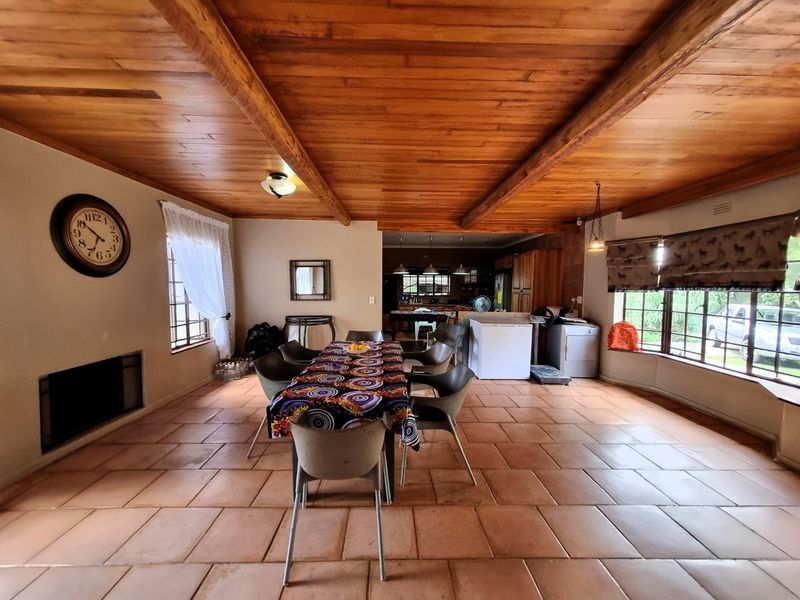 Spacious open-plan living and dining area featuring a warm timber-beamed ceiling, terracotta tiled flooring, and a built-in fireplace, flowing into the kitchen space.