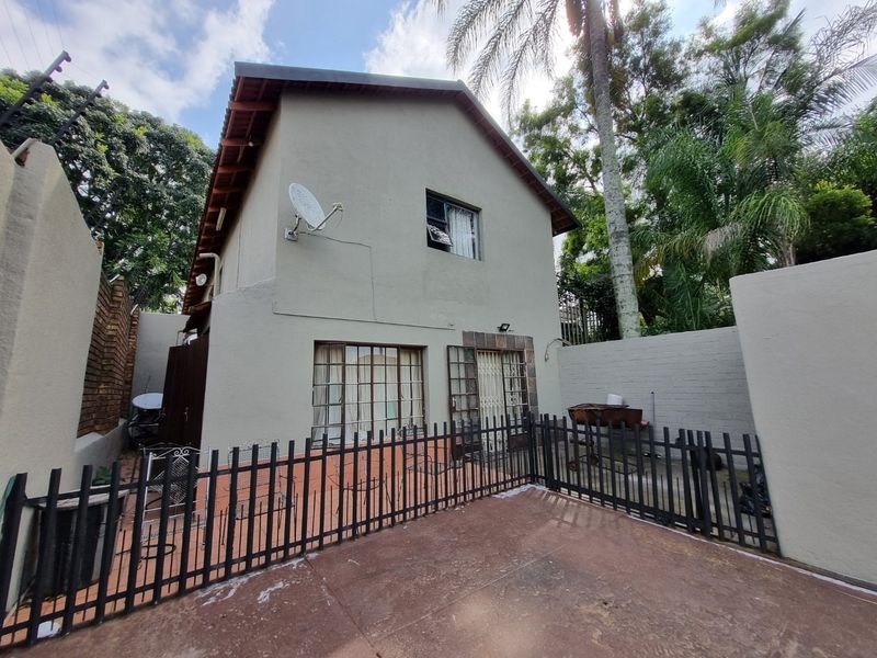 Rear view of the property featuring a paved patio area, security fencing, and a satellite dish mounted on the exterior wall.