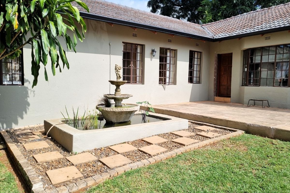 A rear exterior view featuring a paved patio area, a central water feature, and a well-maintained garden space adjacent to the house.