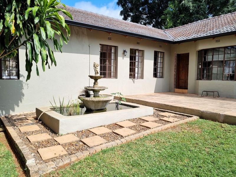 A rear exterior view featuring a paved patio area, a central water feature, and a well-maintained garden space adjacent to the house.