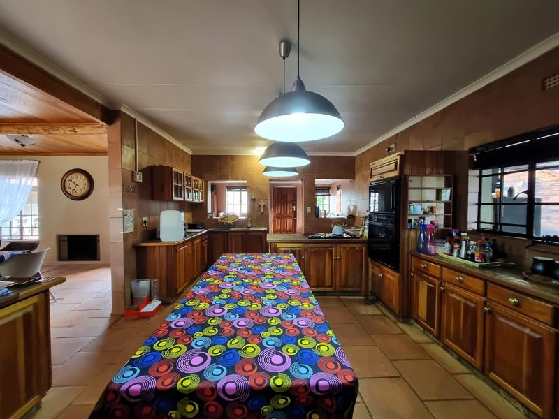 Spacious kitchen featuring extensive wooden cabinetry, tiled flooring, built-in oven and hob, and large pendant lighting, offering a functional layout with classic finishes.
