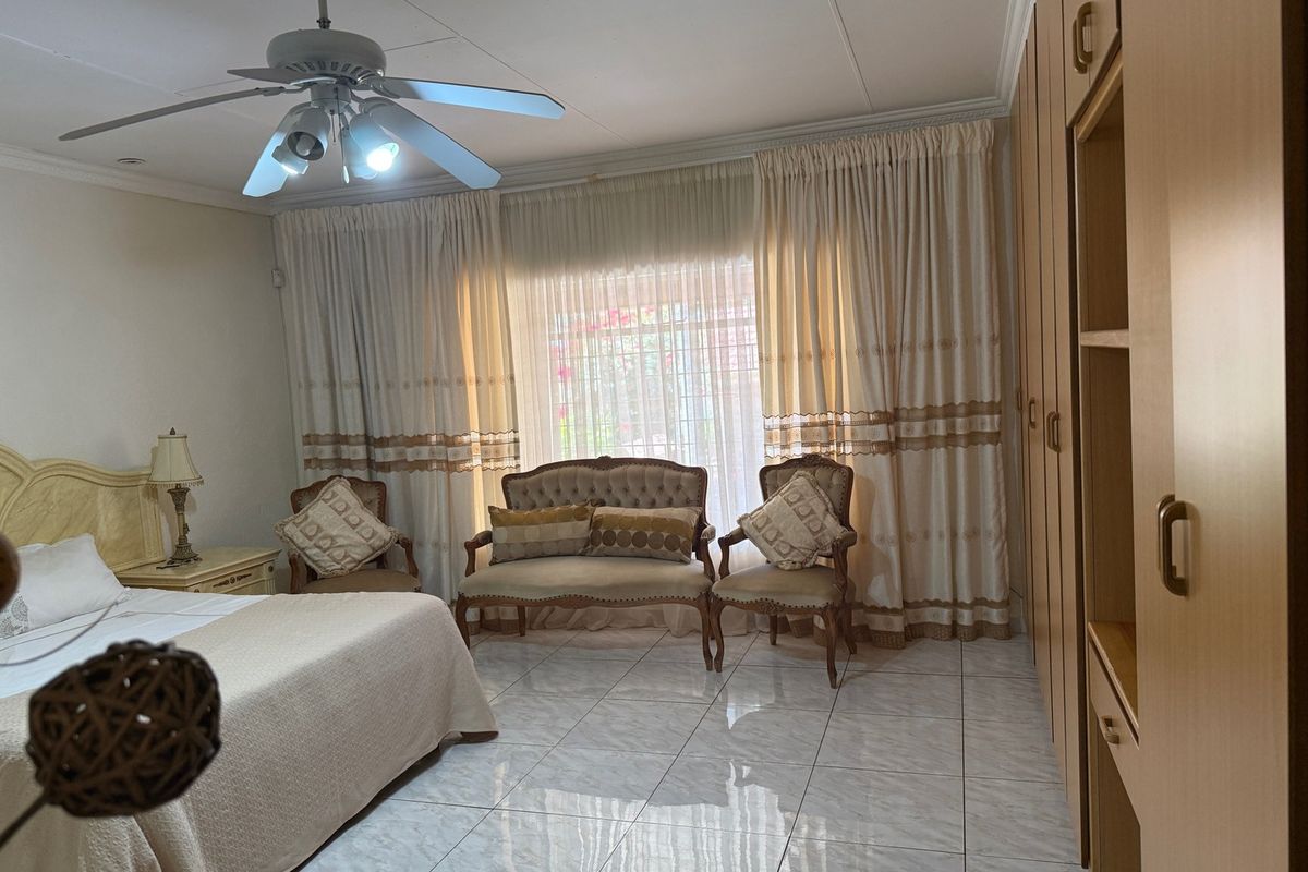 Spacious bedroom featuring tiled flooring, built-in cupboards, and a ceiling fan, offering a comfortable and functional living space.