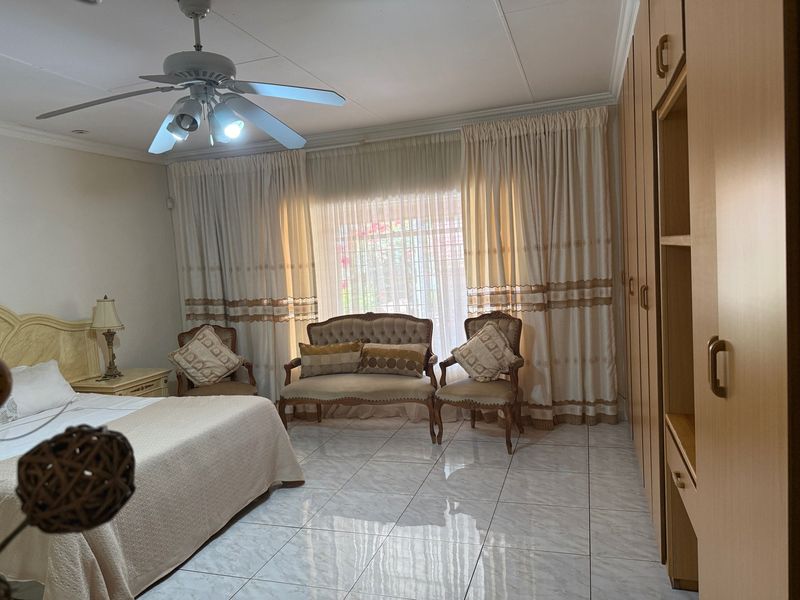 Spacious bedroom featuring tiled flooring, built-in cupboards, and a ceiling fan, offering a comfortable and functional living space.