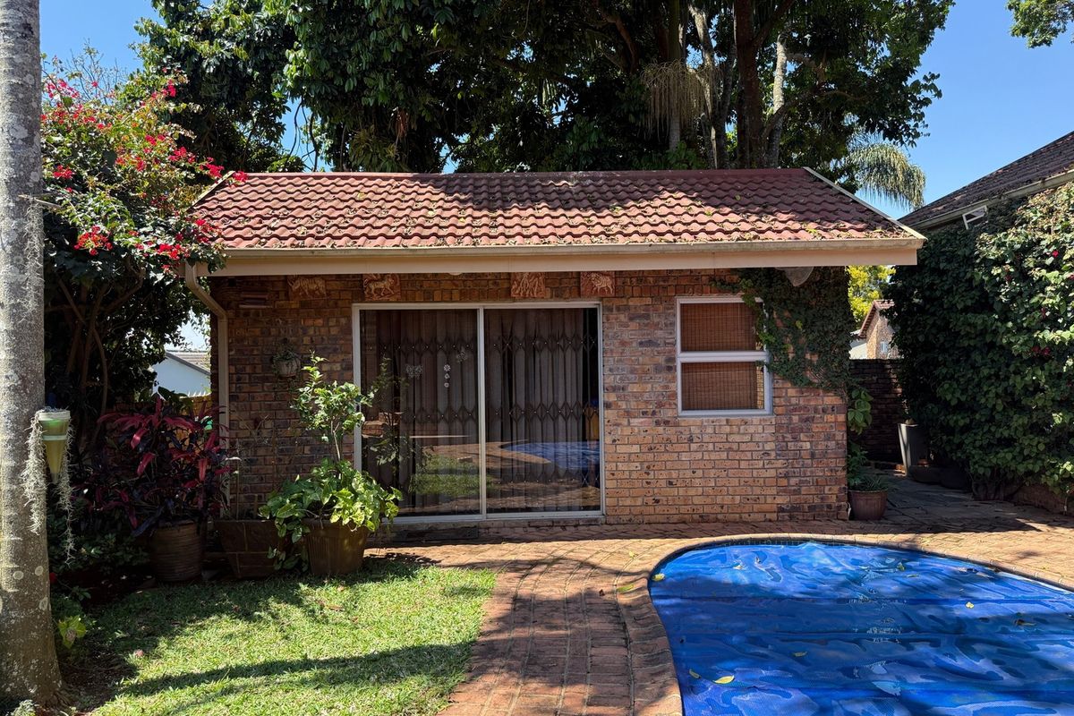 A rear view of a brick outbuilding featuring a tiled roof, sliding glass doors with security gates, and a swimming pool in the foreground.