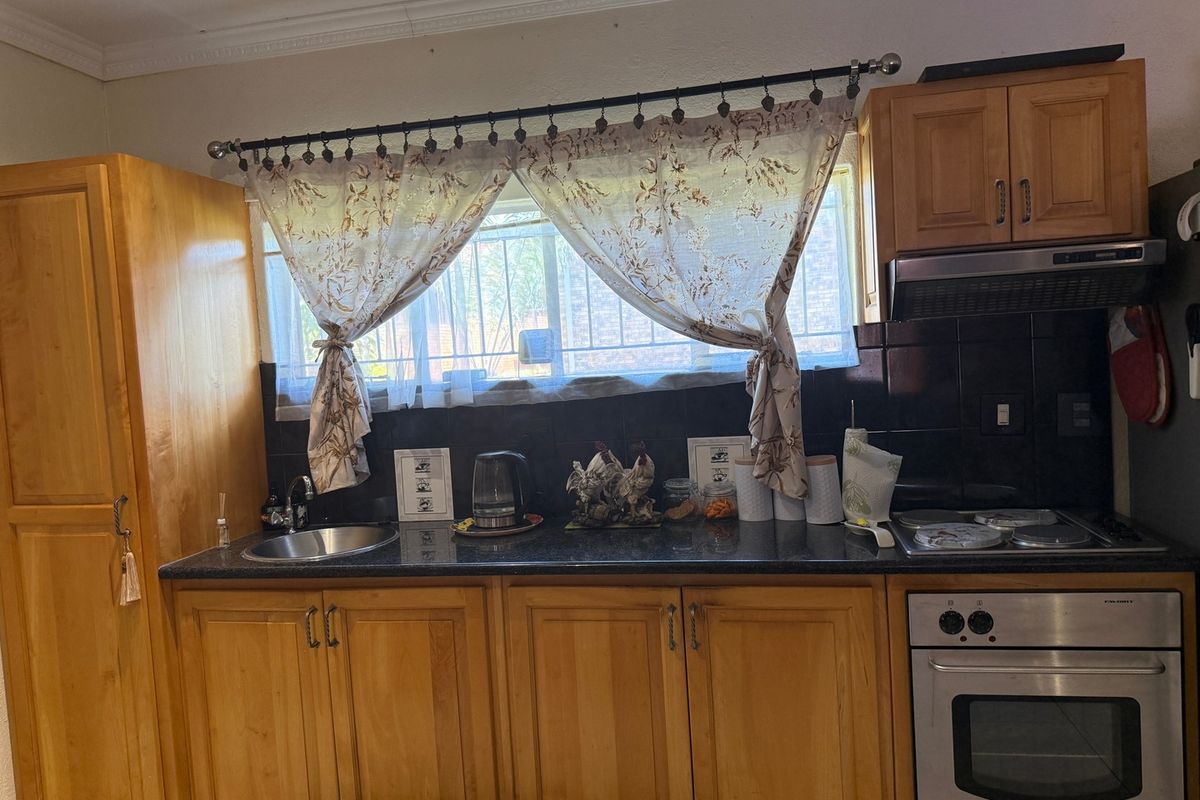 A functional kitchen featuring wooden cabinetry, granite countertops, a stainless steel sink, and built-in cooking appliances with a tiled backsplash.
