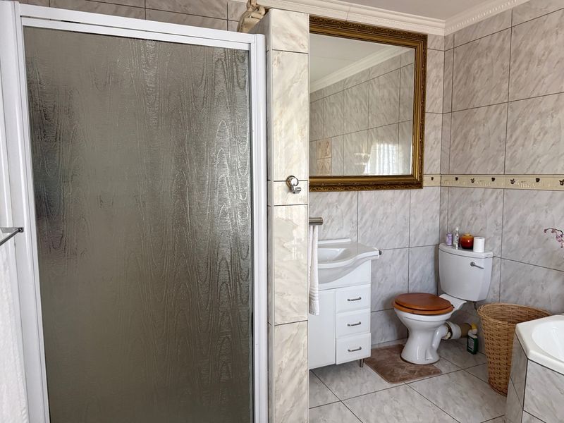 A functional bathroom featuring a shower enclosure, vanity cabinet with washbasin, toilet, and wall-to-wall tiling.