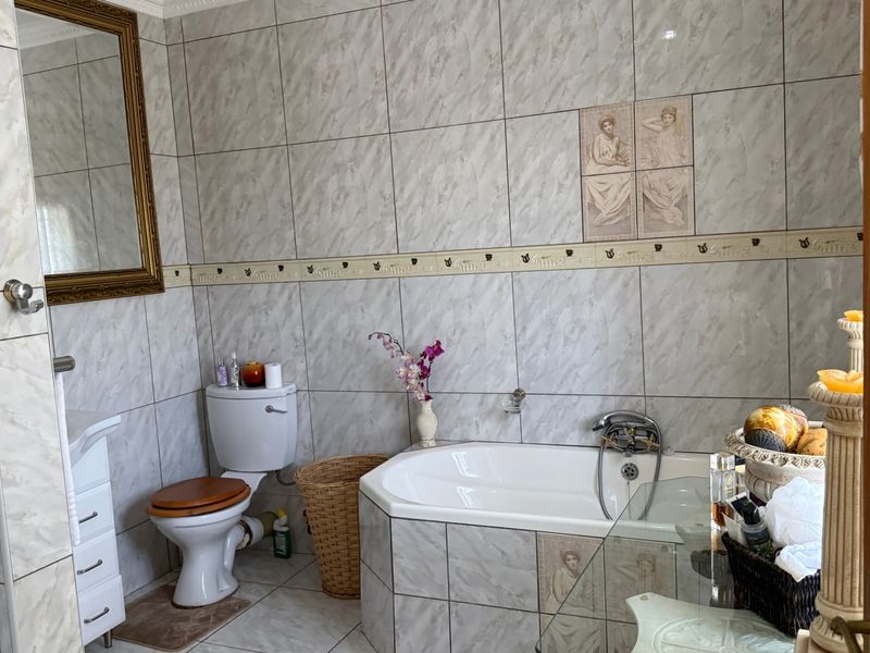 A functional bathroom featuring full-height wall tiling, a built-in bathtub, a vanity unit, and a separate shower enclosure.