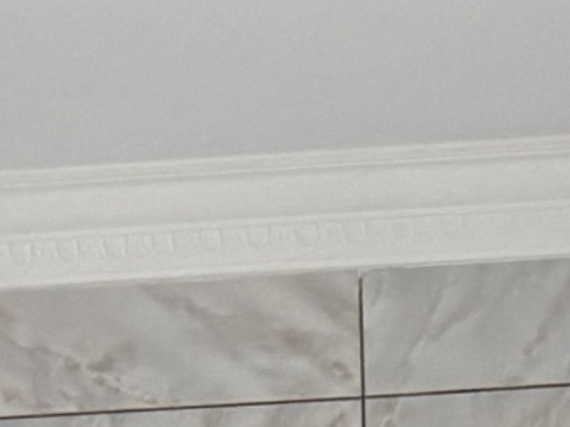 A close-up view showing decorative ceiling cornice and marble-effect wall tiling.