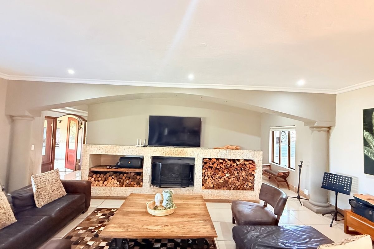 Spacious living room featuring a prominent built-in stone fireplace with integrated wood storage, decorative columns, and an arched architectural detail.