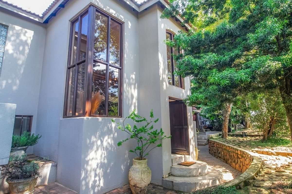 A view of the rear exterior featuring large timber-framed windows, a stone retaining wall, and a paved pathway leading to a timber entrance door.