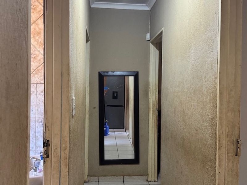 A narrow interior hallway featuring tiled flooring and coving, currently showing significant wear and staining on the wall surfaces.