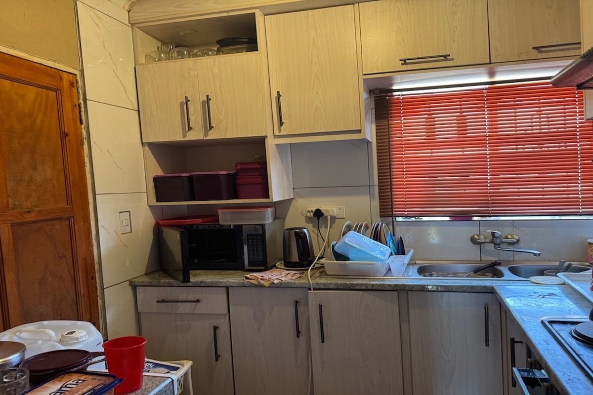 A functional kitchen featuring light-toned built-in cabinetry, laminate countertops, a stainless steel double sink, and an integrated electric hob with a tiled backsplash.