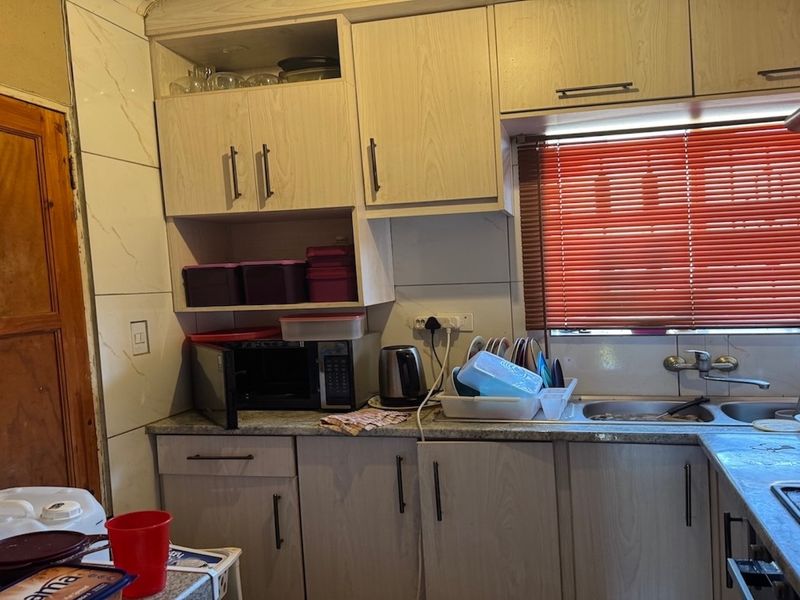 A functional kitchen featuring light-toned built-in cabinetry, laminate countertops, a stainless steel double sink, and an integrated electric hob with a tiled backsplash.