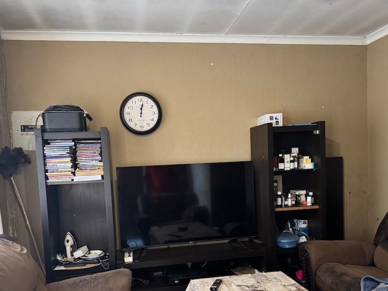 A living room area featuring a visible electrical distribution board and standard wall finishes, currently showing signs of wear on the walls and ceiling.