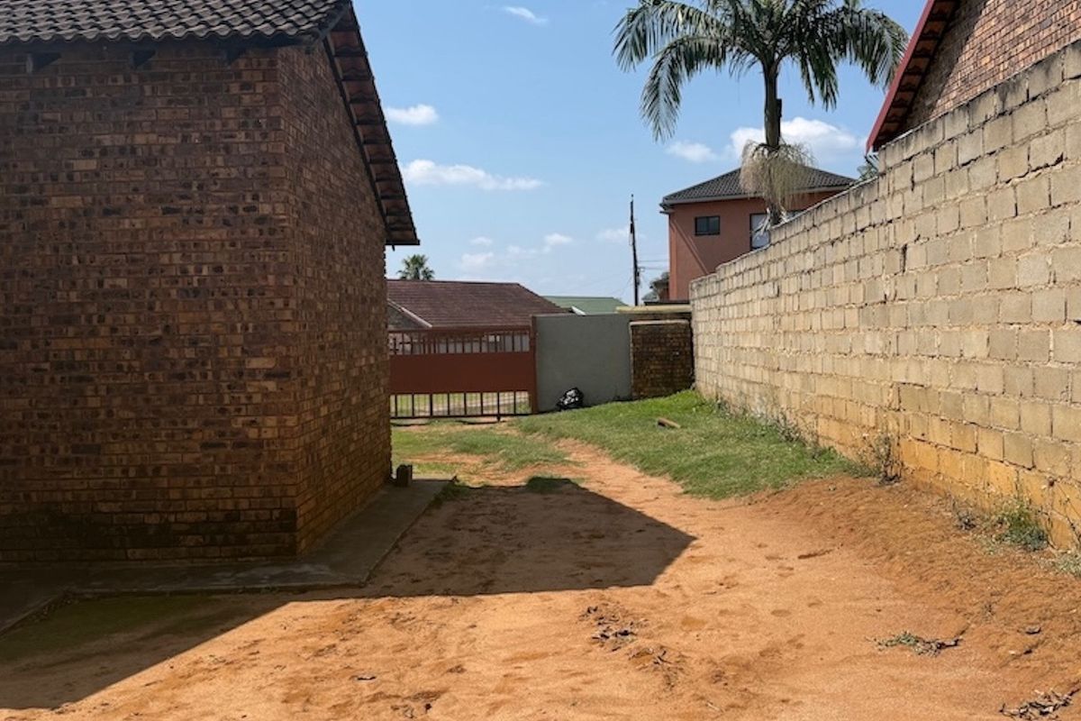 A view of the rear exterior area featuring a face brick building, a concrete block boundary wall, and an unpaved yard space.