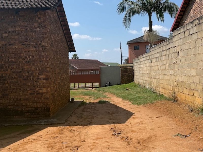 A view of the rear exterior area featuring a face brick building, a concrete block boundary wall, and an unpaved yard space.