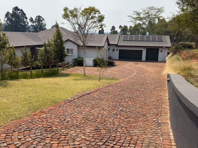 A well-maintained front exterior featuring a curved cobblestone driveway, double garage, and solar panel installation on a modern metal roof.