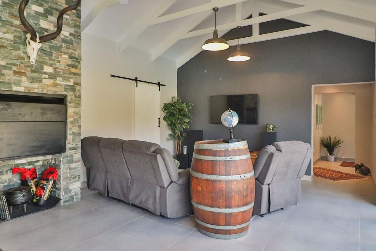 Spacious living room featuring a vaulted ceiling with exposed trusses, a striking stone-clad fireplace, and modern tiled flooring.
