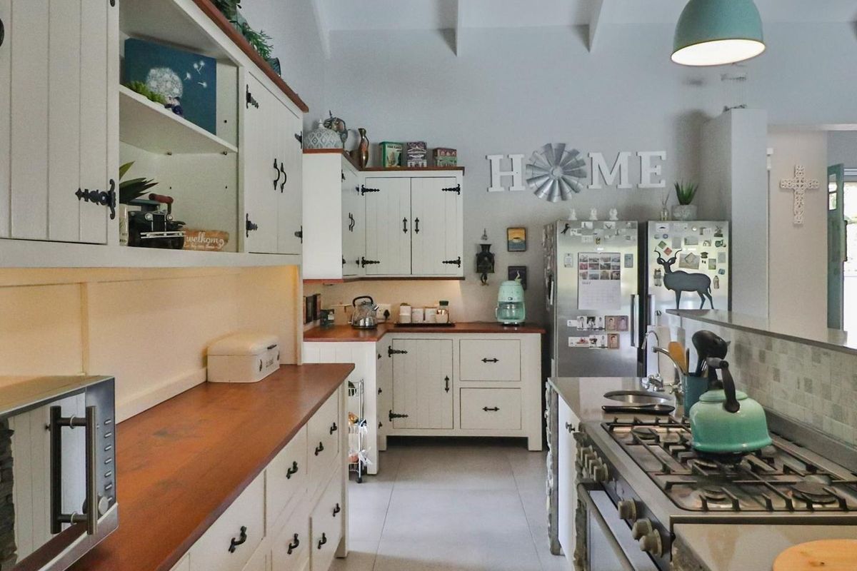 A well-maintained kitchen featuring white cabinetry, warm wooden countertops, a gas hob, and integrated appliances with a bright, functional layout.