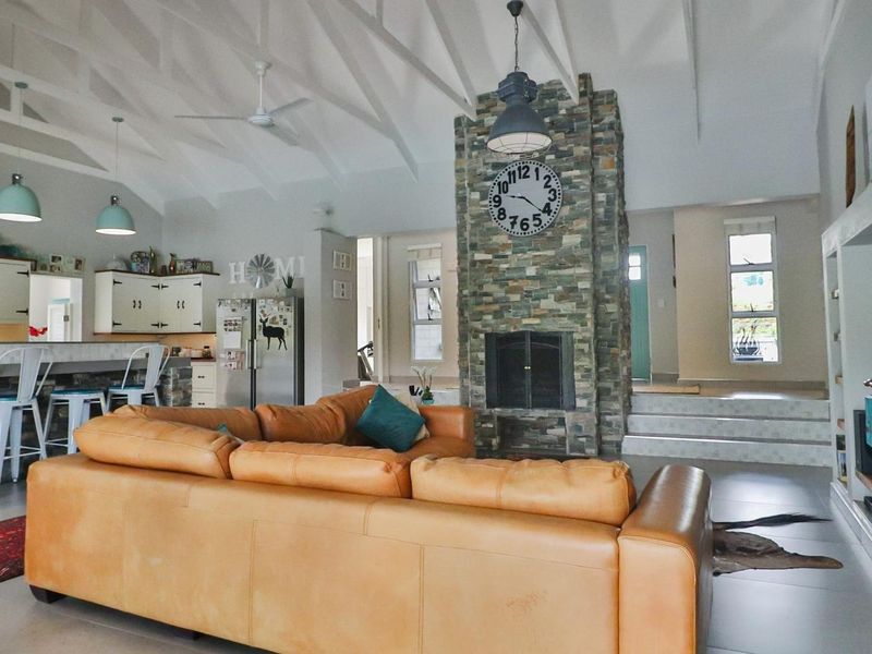 Spacious open-plan living area featuring a striking stone-clad fireplace, vaulted ceilings, and a functional kitchen with a breakfast bar.