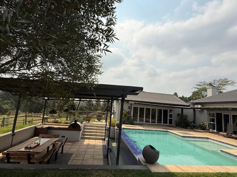 Spacious outdoor entertainment area featuring a swimming pool, covered patio with built-in braai, and views of the surrounding landscape.